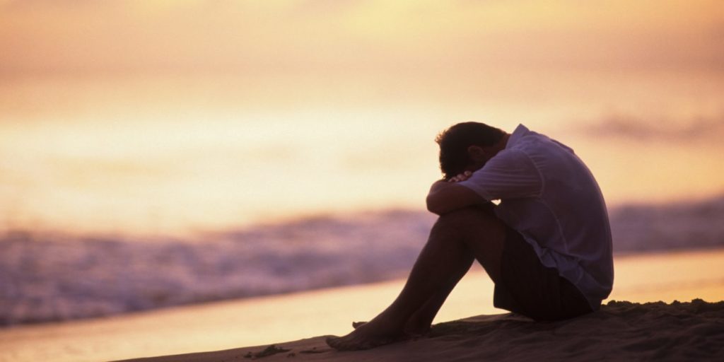 Man hugging knees on beach at sunset